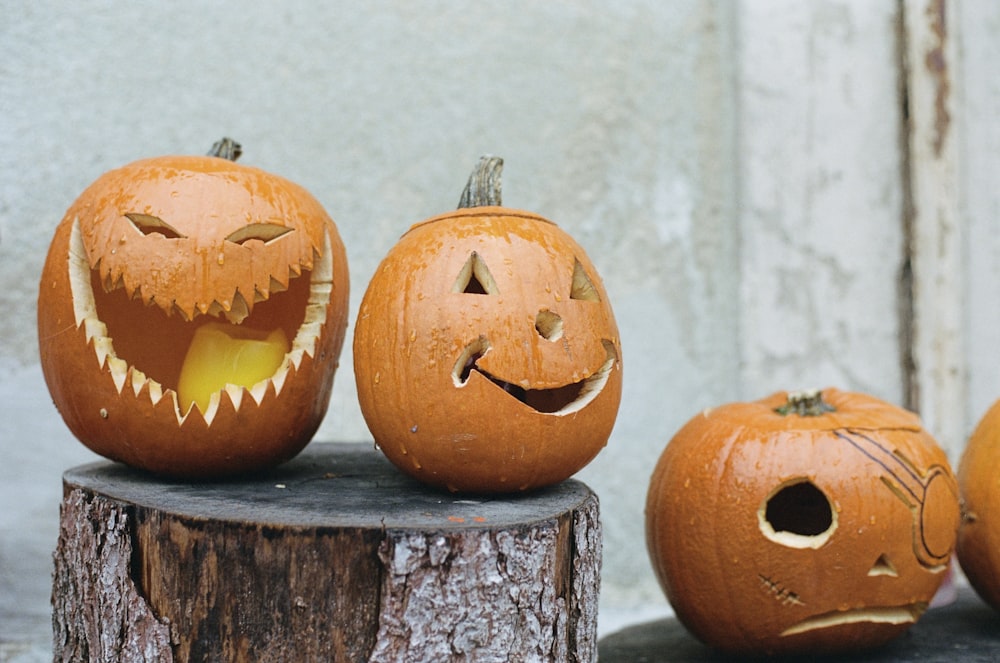 three carved pumpkins sitting on top of a tree stump