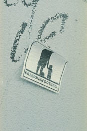 A weathered sticker is affixed to a rough-textured surface, depicting the silhouette of an adult holding hands with a child, next to a soccer ball. The words 'PASSION & FOOTBALL' are printed below the figures, suggesting a connection between family and the sport.