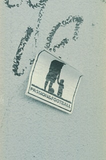 A weathered sticker is affixed to a rough-textured surface, depicting the silhouette of an adult holding hands with a child, next to a soccer ball. The words 'PASSION & FOOTBALL' are printed below the figures, suggesting a connection between family and the sport.