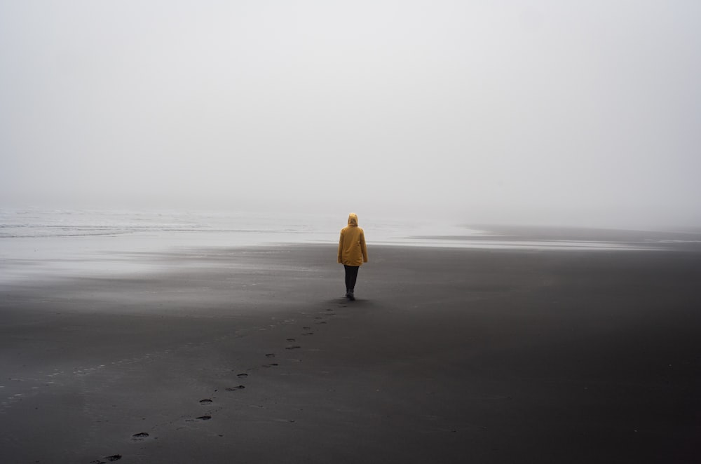 Una persona con una chaqueta amarilla caminando en una playa
