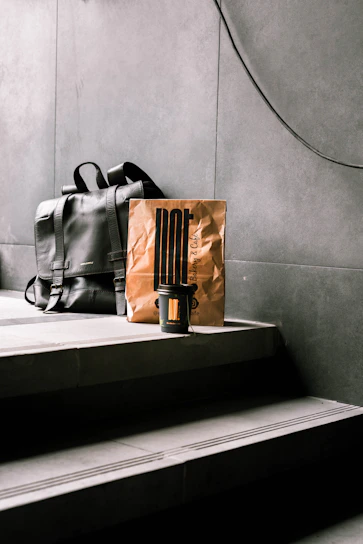 Architectural shot of a minimalist travel bag placed against a concrete wall with strong shadows and orange industrial accents.