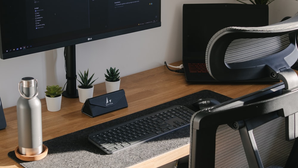 a desk with a computer monitor, keyboard, mouse and a plant