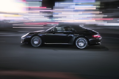 Sleek black sports car speeding through Caracas streets at dusk with city lights blurred.