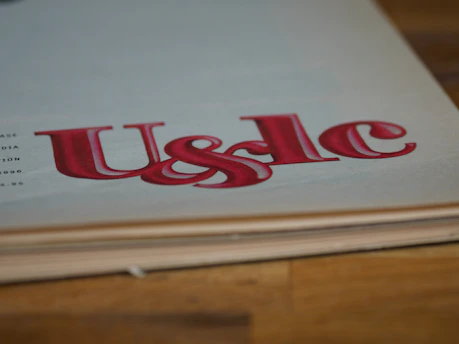 Large, stylized red lettering 'U&lc' on the corner of a page, with the edge of a book in the foreground and a wooden surface underneath.