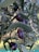 Dark purple olives hang from a branch surrounded by slender green leaves. The sunlight filters through the foliage, casting gentle shadows and highlights on the olives, enhancing their glossy texture.