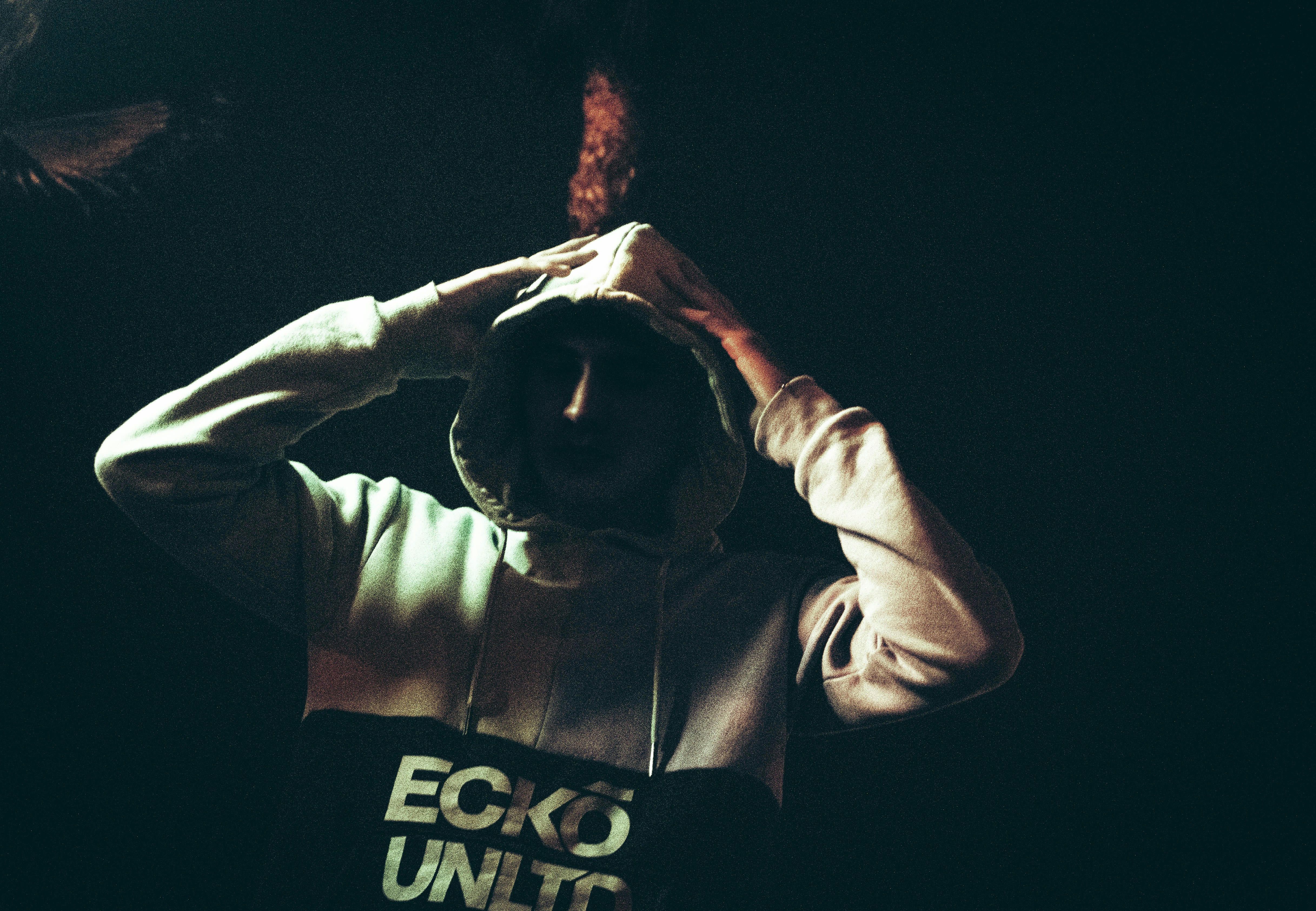 a man in a hoodie holding his hands up to his head