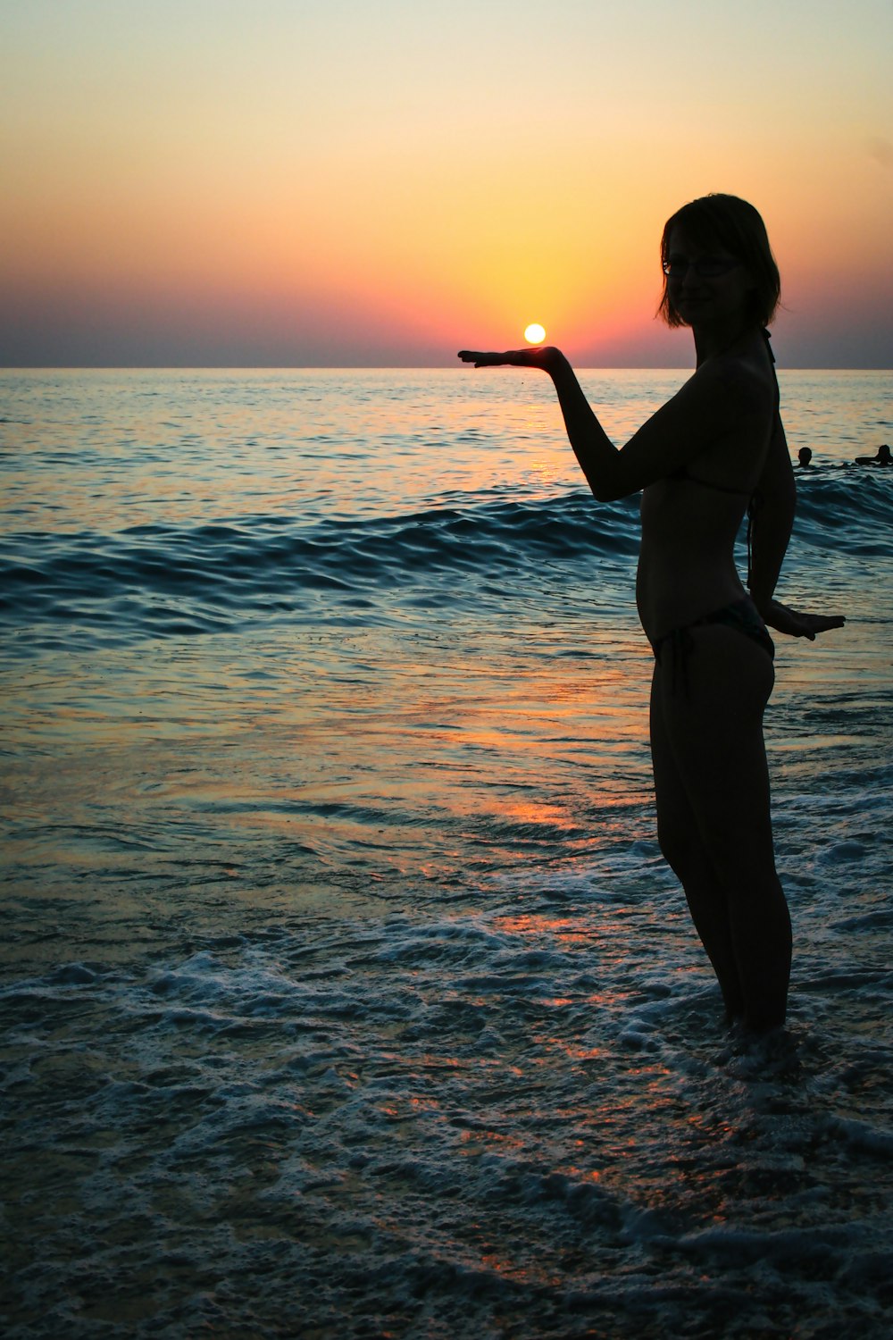 a woman standing in the ocean at sunset