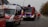 Several fire department vehicles are parked on a residential street, including a fire truck and an emergency response van. A group of firefighters dressed in uniforms and helmets are standing near the vehicles, appearing to be in communication or preparing for action. The scene takes place on an overcast day, with trees without leaves visible in the background.