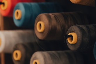 Large spools of thread arranged in a row, showcasing various colors including blue, grey, and beige. Each spool has a yellow central spool core, providing contrast against the threads.