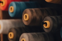 Large spools of thread arranged in a row, showcasing various colors including blue, grey, and beige. Each spool has a yellow central spool core, providing contrast against the threads.