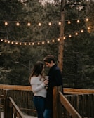 A couple enjoying a private candlelit dinner on a wooden deck above crystal-clear water.