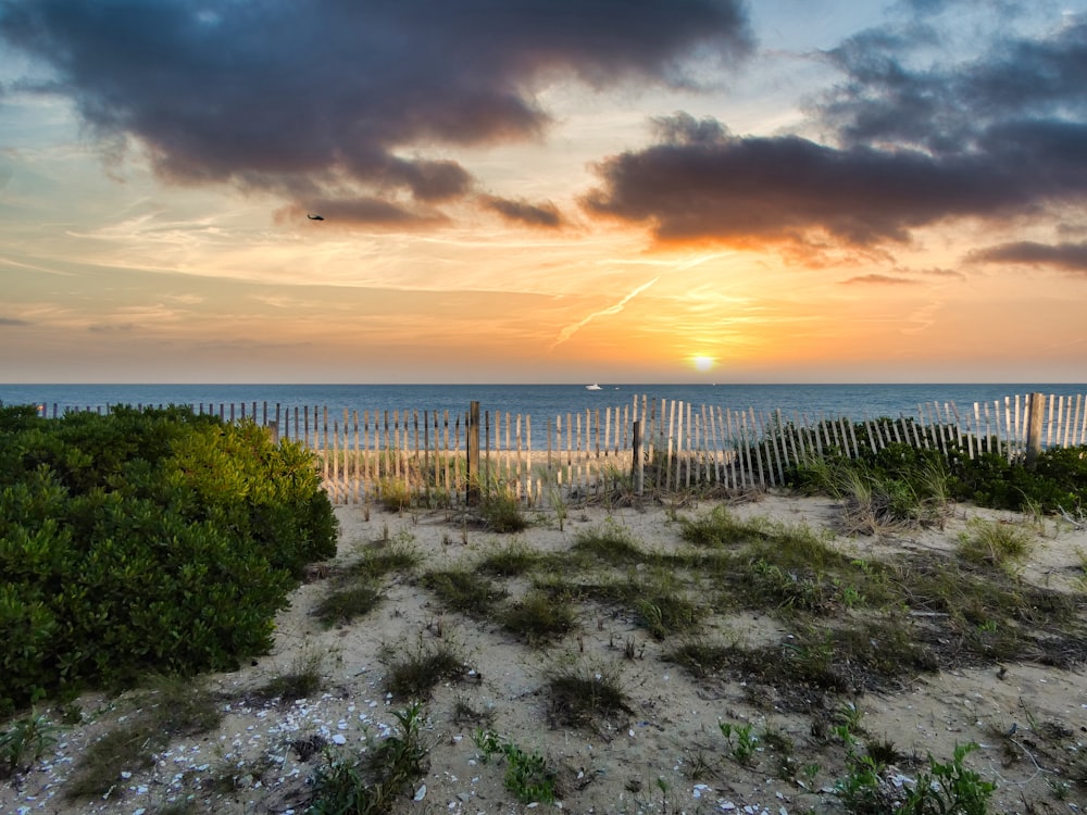 the sun is setting over the beach with a fence