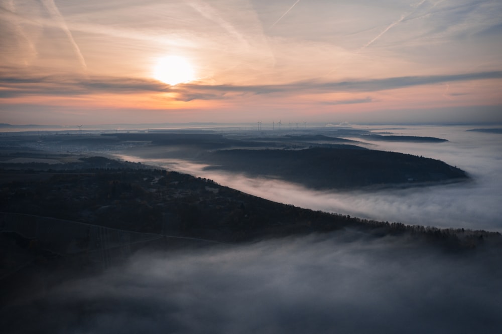 the sun is setting over a foggy valley