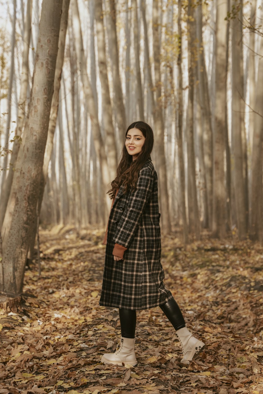 a woman standing in a forest with leaves on the ground