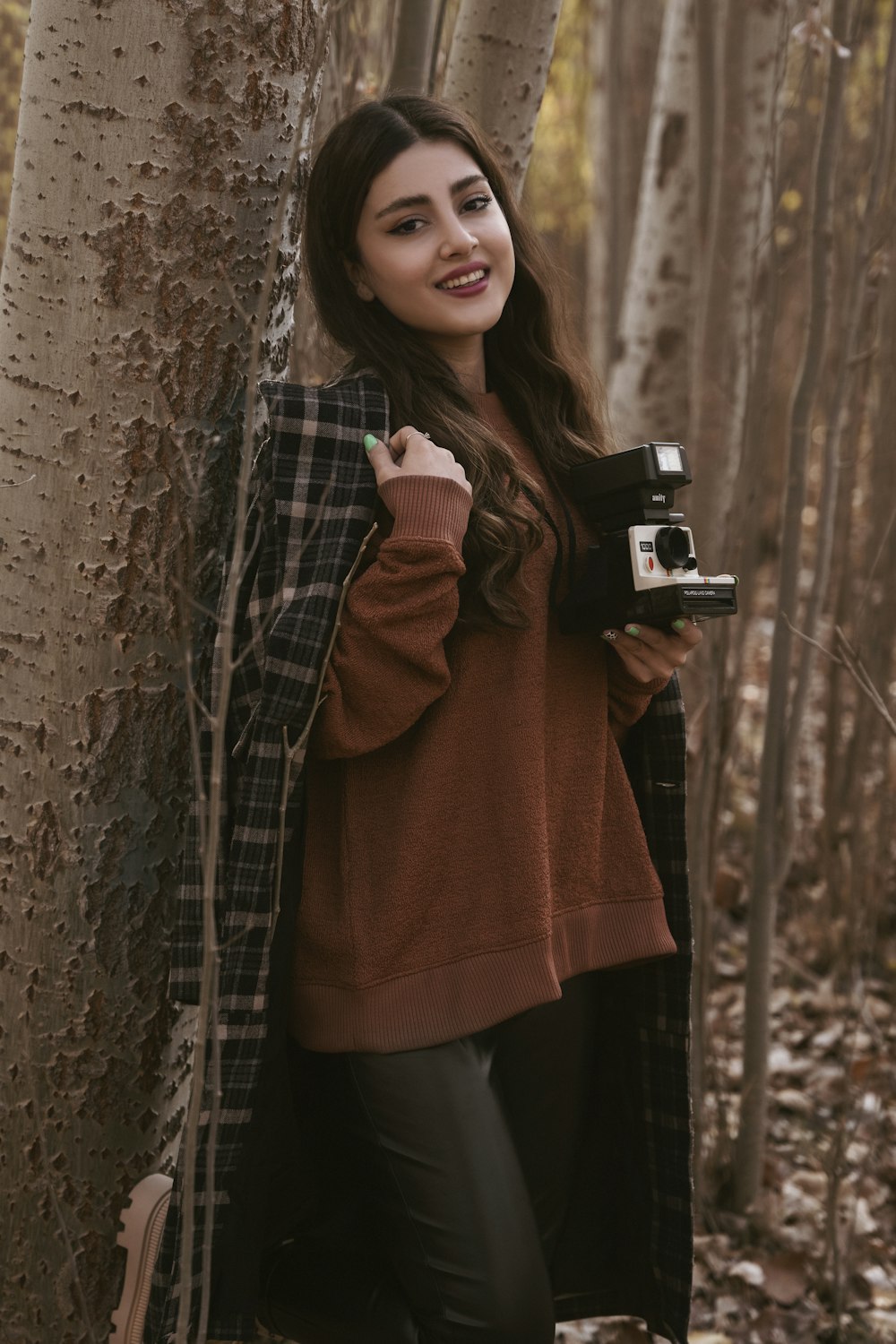 a woman standing next to a tree holding a camera