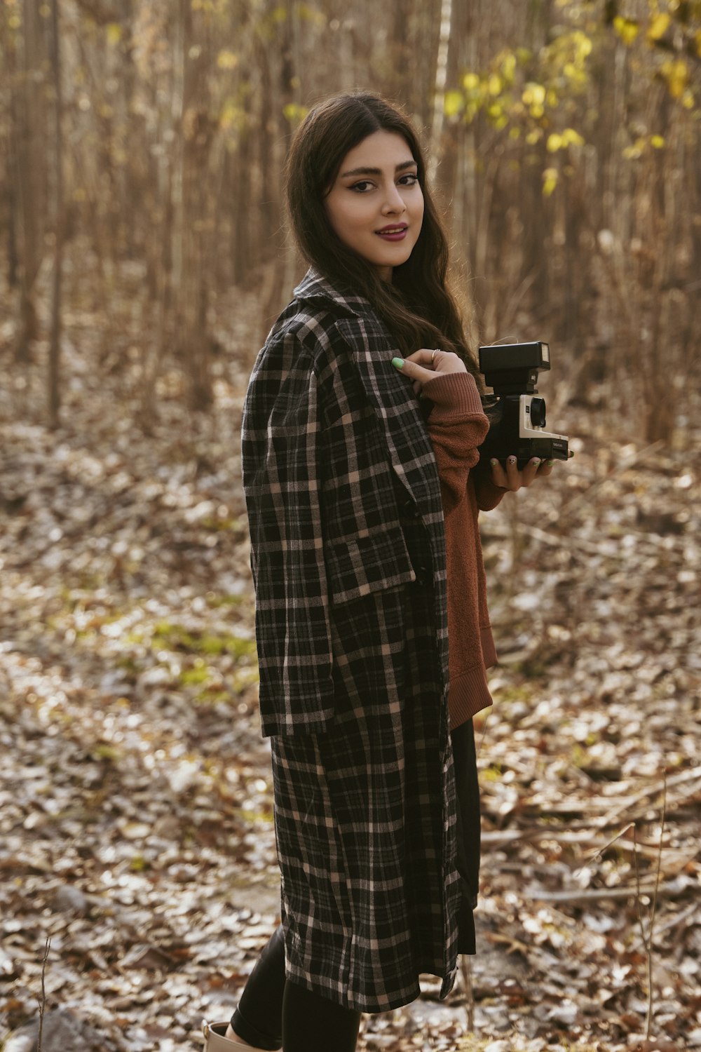 a woman standing in the woods holding a camera