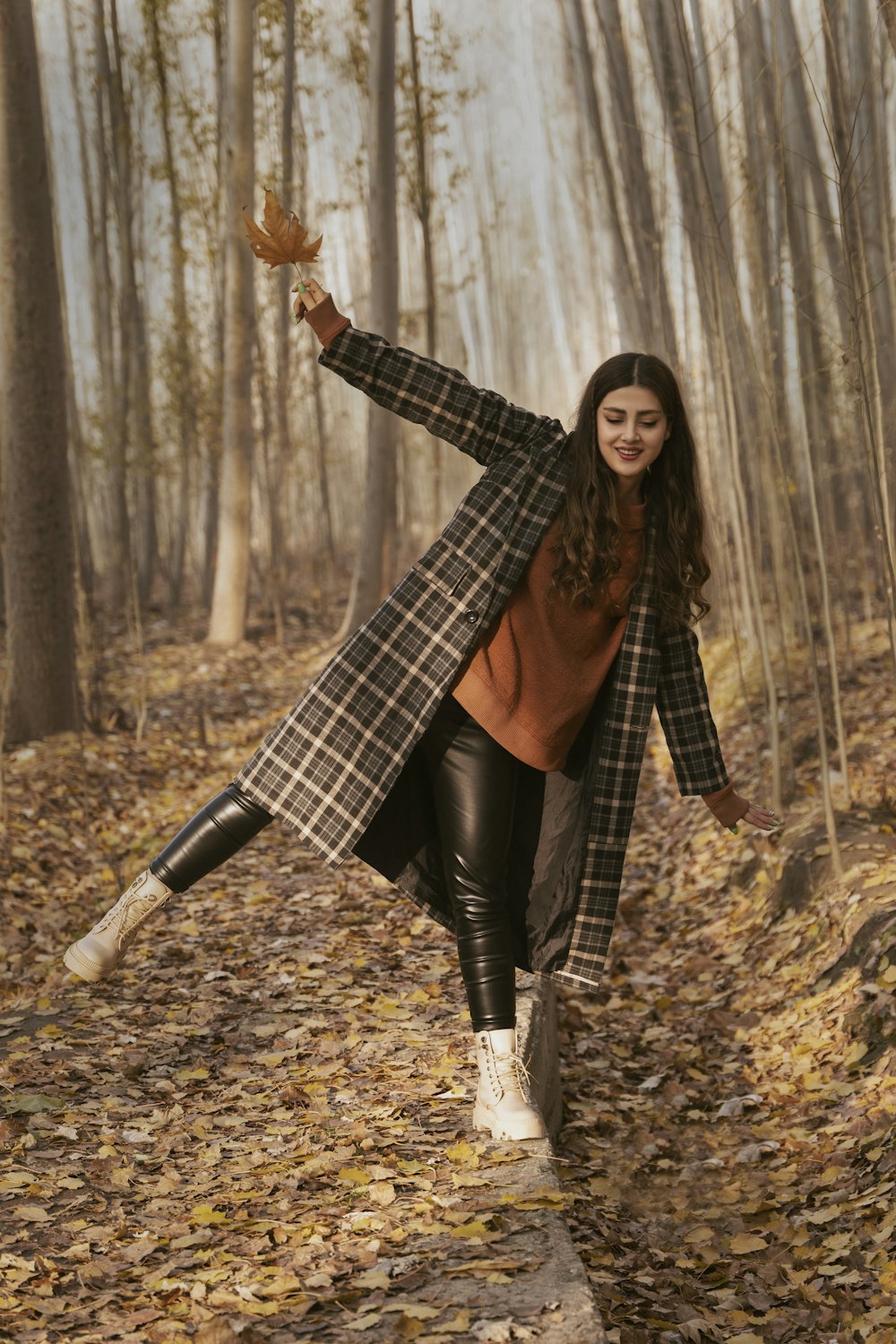 a woman in a plaid coat is walking through the woods