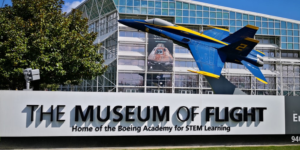 a blue and yellow fighter jet flying over a museum of flight sign