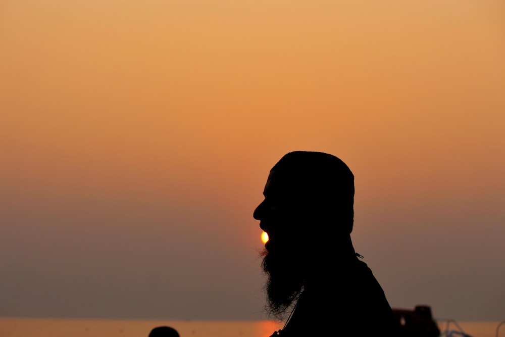 a man with a long beard standing in front of a sunset