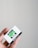 A close-up of a hand holding a box of Ilford HP5 Plus black and white film against a plain light-colored background. The box is primarily white with bold black and green text showcasing the brand and type of film.