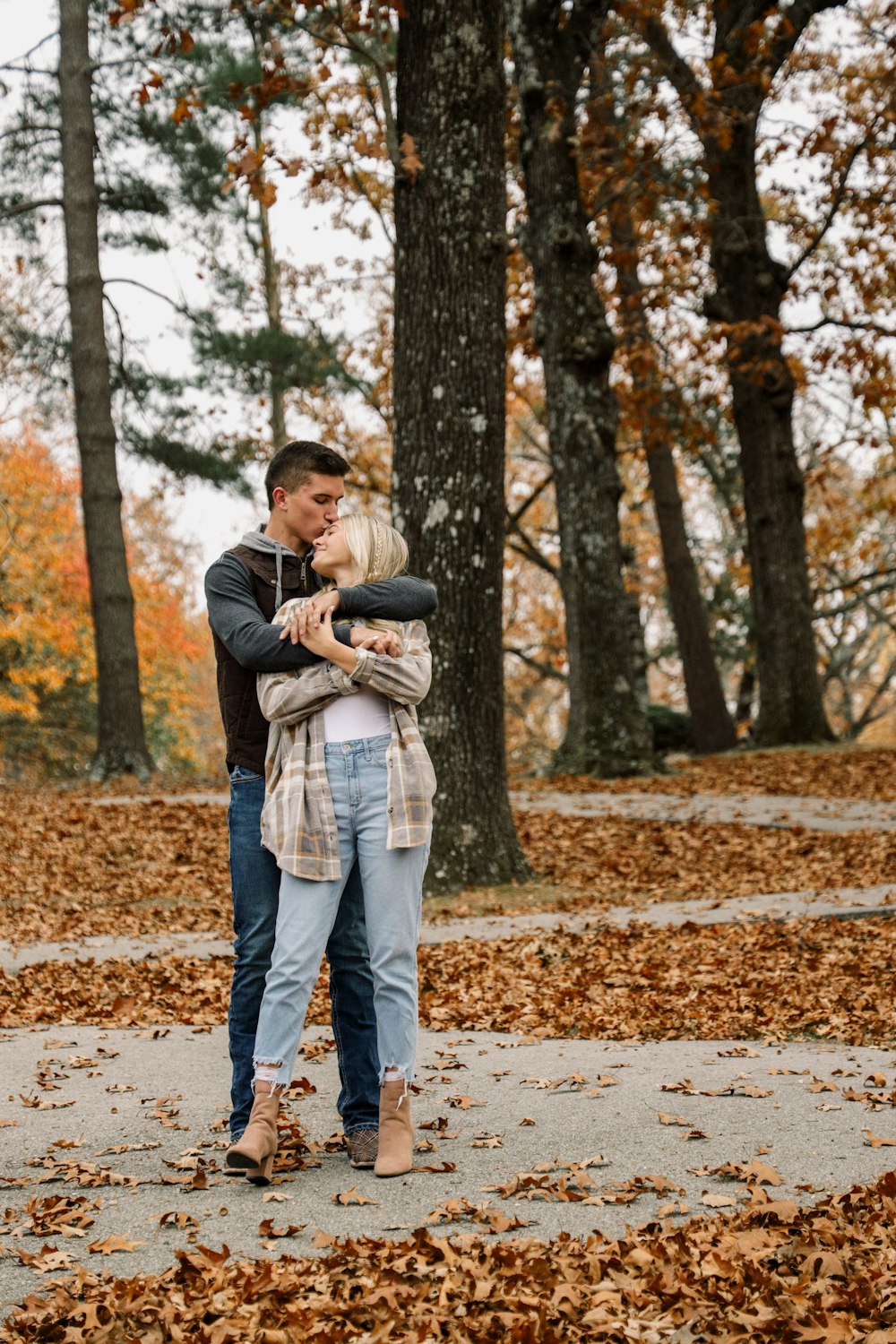 a man holding a woman in a park with leaves on the ground