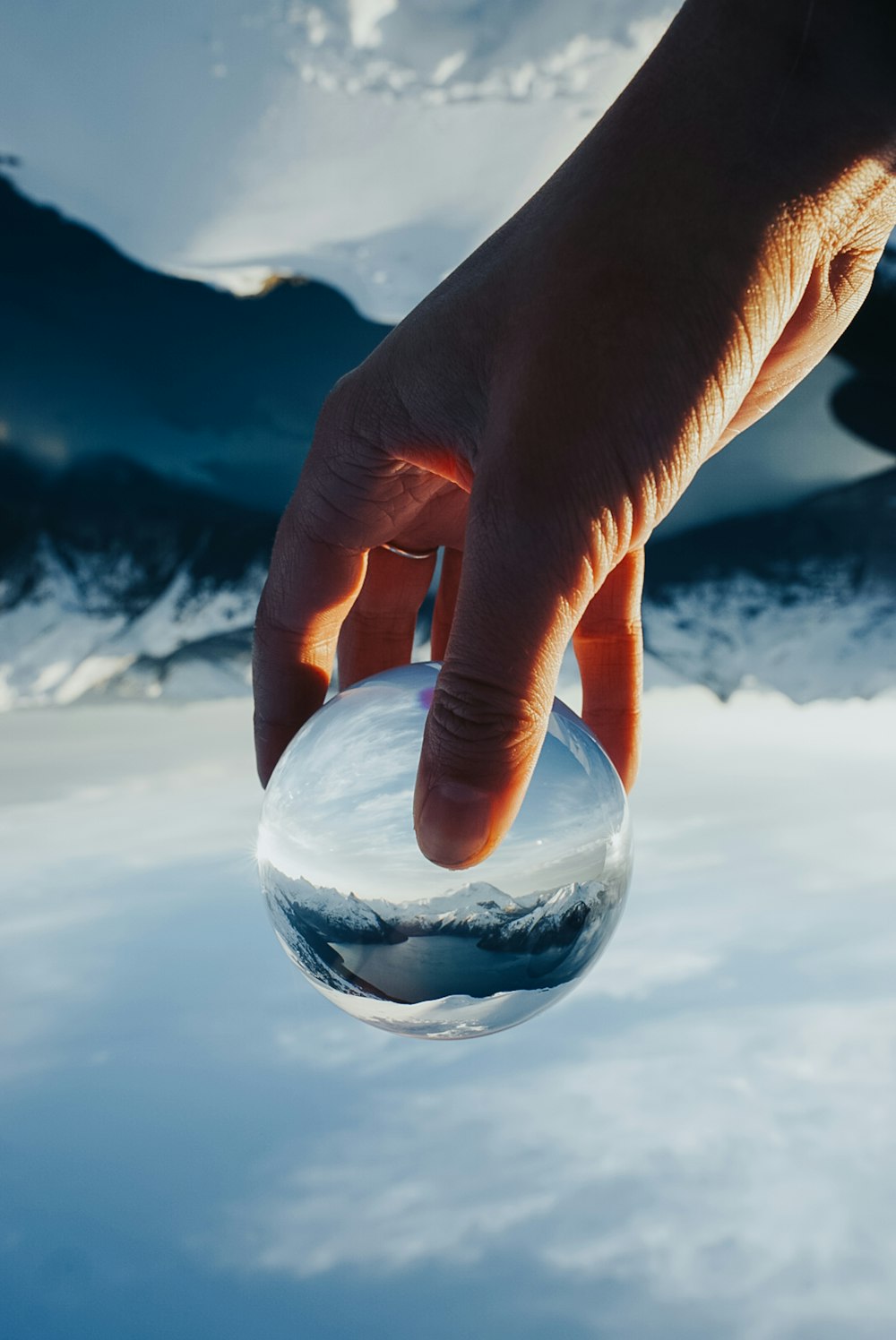 a person's hand touching a glass ball in the snow