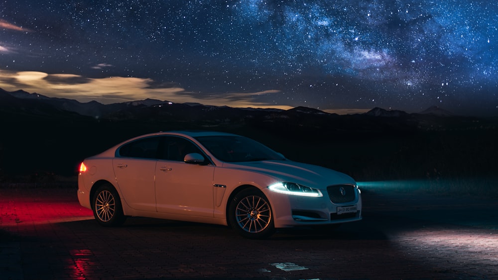 a white car parked in front of a night sky filled with stars