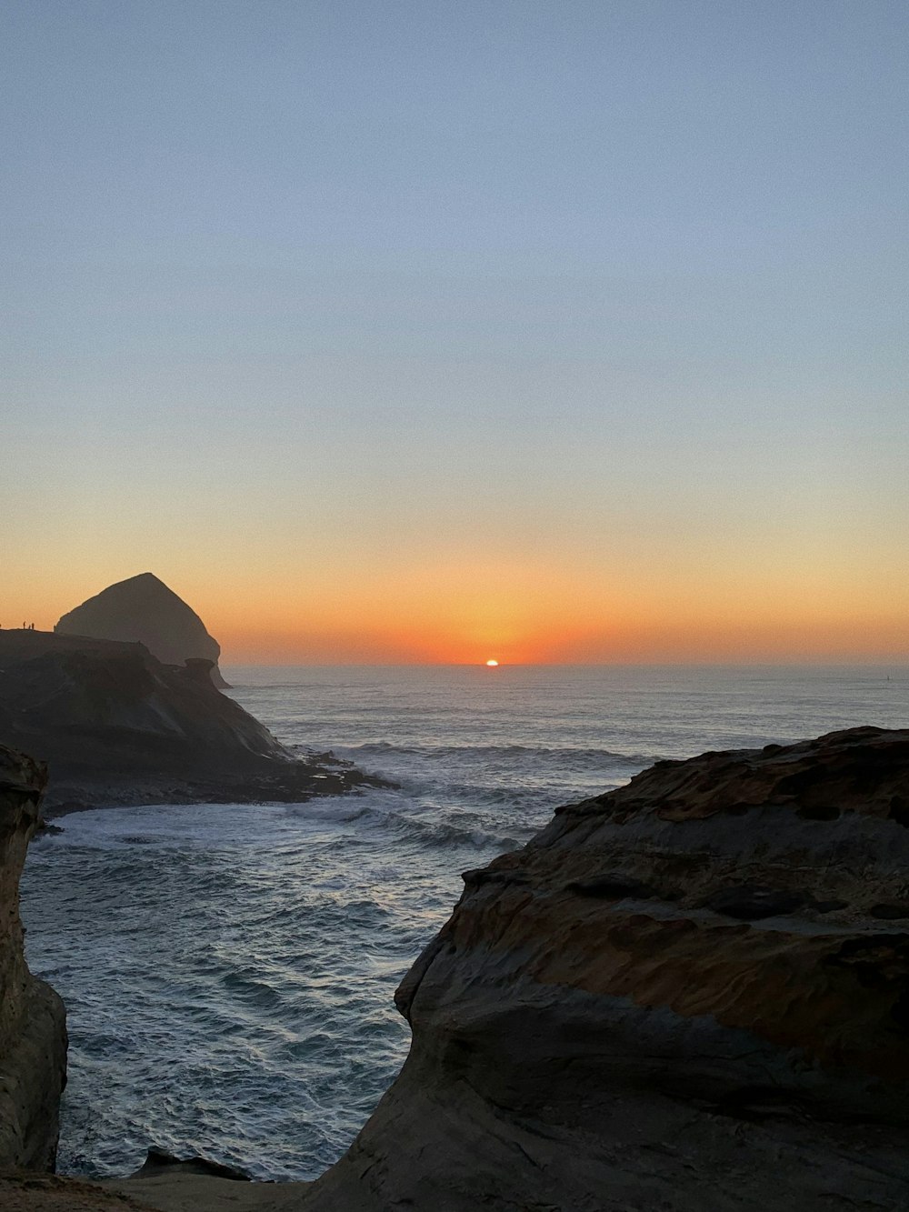 the sun is setting over the ocean and rocks