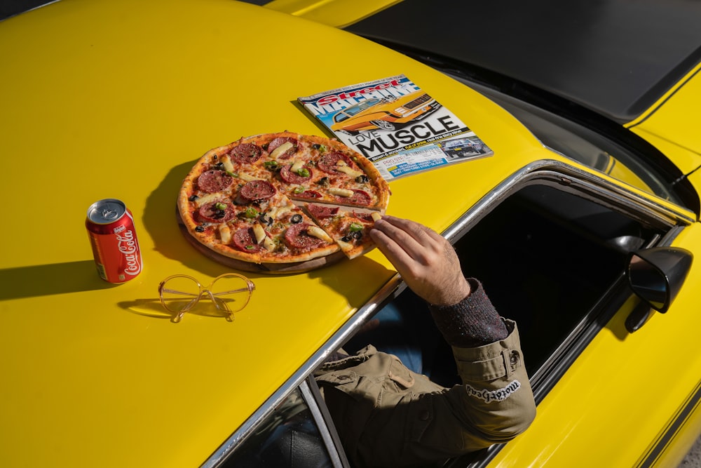 a man holding a pizza on top of a yellow car