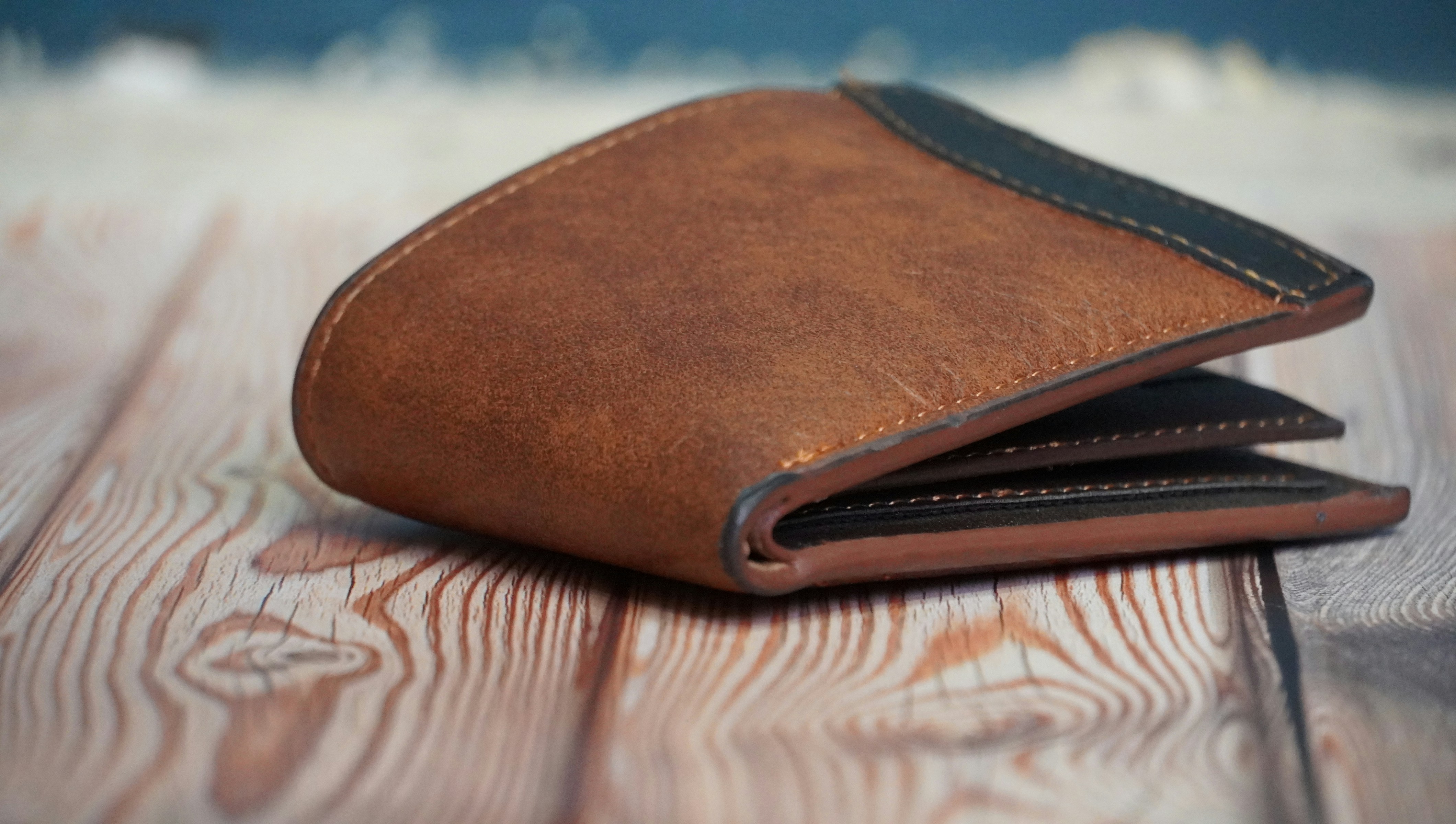 Brown genuine leather bifold wallet on wooden surface