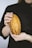 A pair of hands carefully holding a ripe, marbled yellow and brown cocoa pod against a dark background.