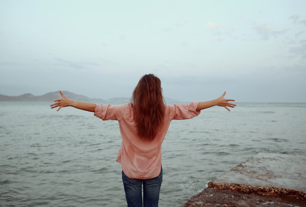 a woman standing on the edge of a cliff by the water