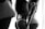 Black and white photo of two women standing closely together, with their backs to the camera. They are wearing lacy underwear, one in a black set and the other in a white set. The lighting creates a soft, intimate atmosphere.