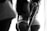 Black and white photo of two women standing closely together, with their backs to the camera. They are wearing lacy underwear, one in a black set and the other in a white set. The lighting creates a soft, intimate atmosphere.