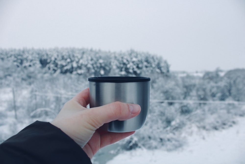 a person holding a cup in front of a snowy landscape