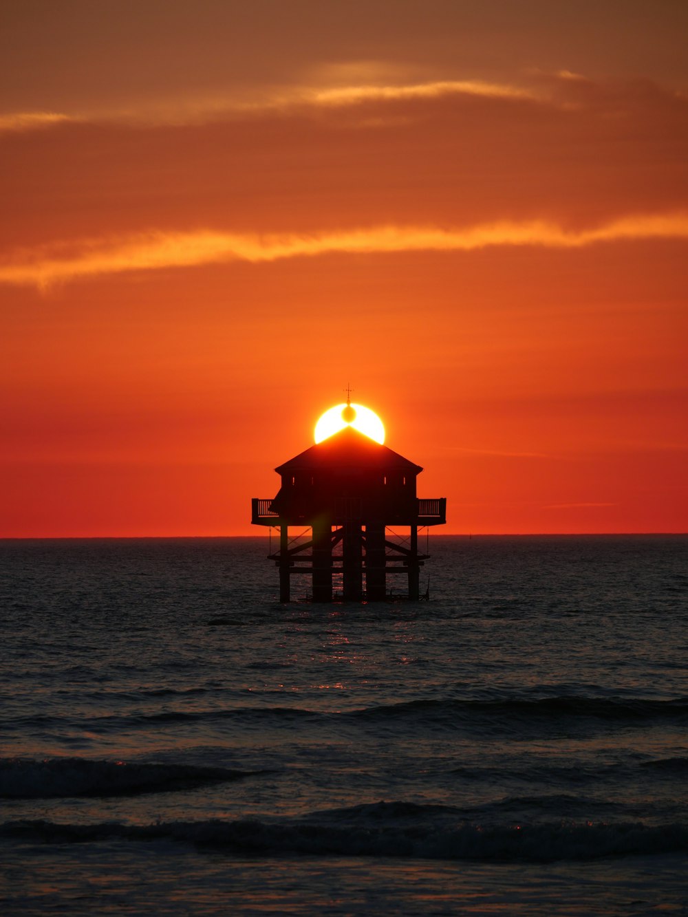 the sun is setting over the ocean with a small building in the foreground