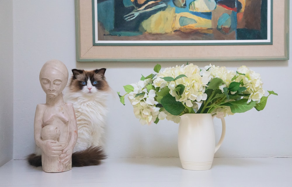 꽃이 든 꽃병 옆 테이블에 앉아 있는 고양이