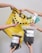 Multiple hands are holding various gardening and plant care products such as soil bags, plant nutrients, a spray bottle, and small bottles with liquids against a plain background with a yellow shopping bag.