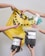 Multiple hands are holding various gardening and plant care products such as soil bags, plant nutrients, a spray bottle, and small bottles with liquids against a plain background with a yellow shopping bag.