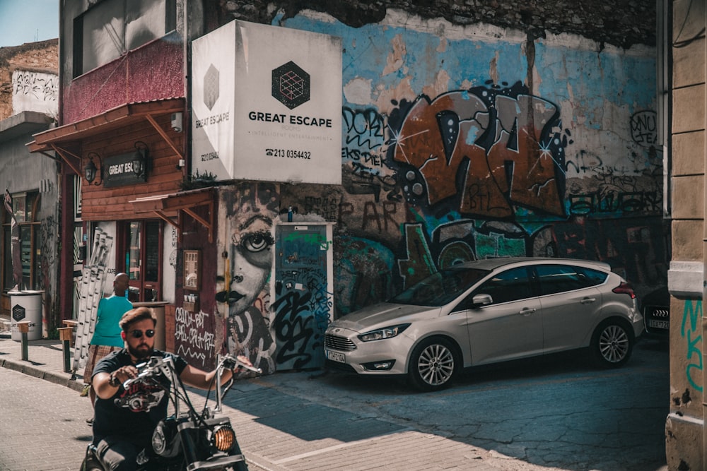 a man riding a motorcycle down a street next to a parked car