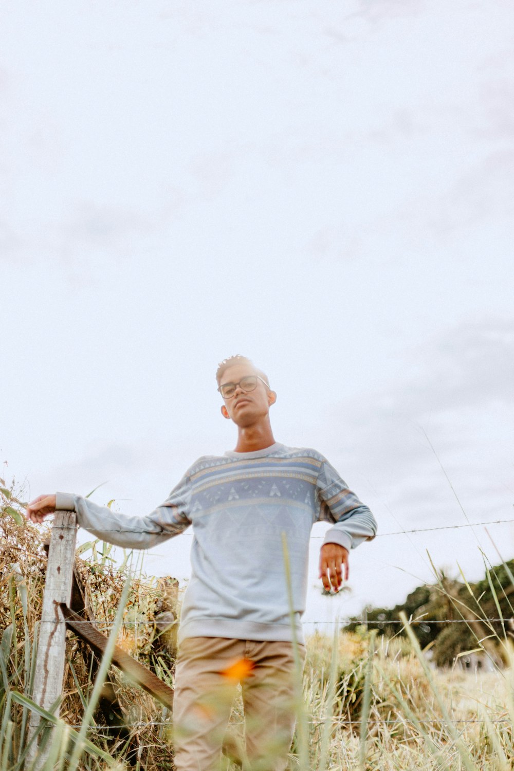 a man standing in tall grass next to a fence