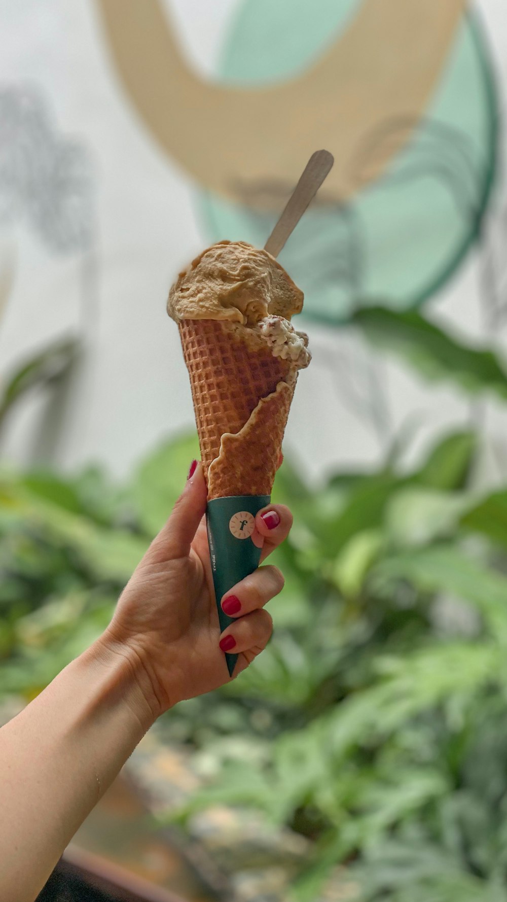a hand holding an ice cream cone with a spoon in it