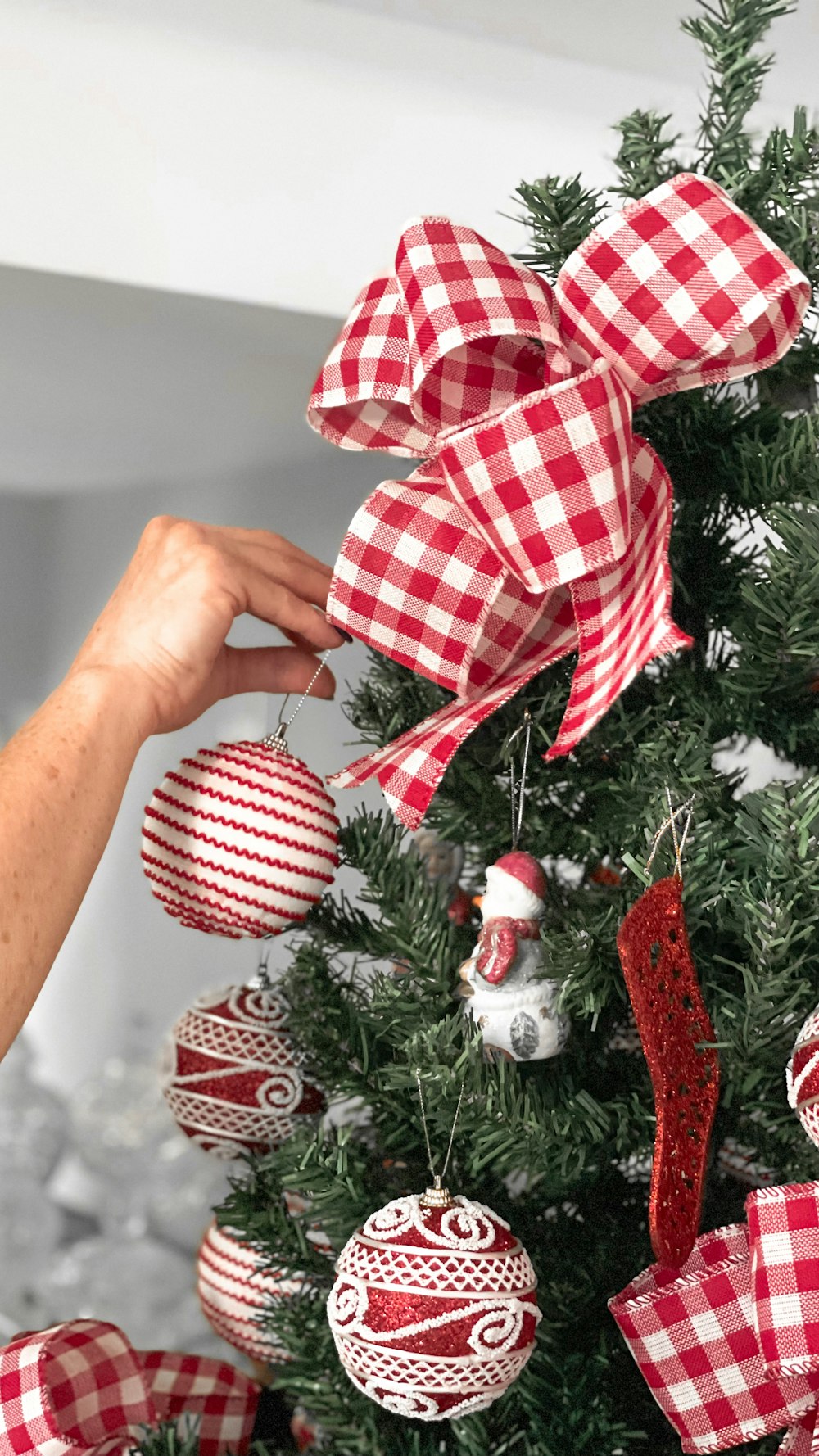 a person decorating a christmas tree with red and white ornaments