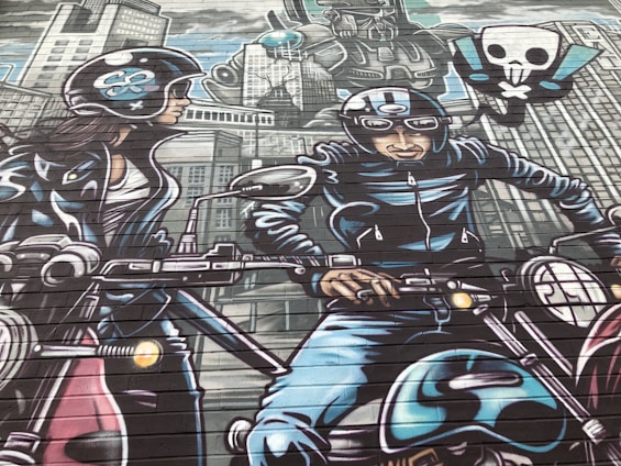 A vibrant mural depicts two motorcyclists wearing helmets and leather gear, riding through a stylized cityscape. The background features tall buildings and a large robot with a skull and crossbones symbol. The mural uses a comic book style with bold outlines and dynamic poses.