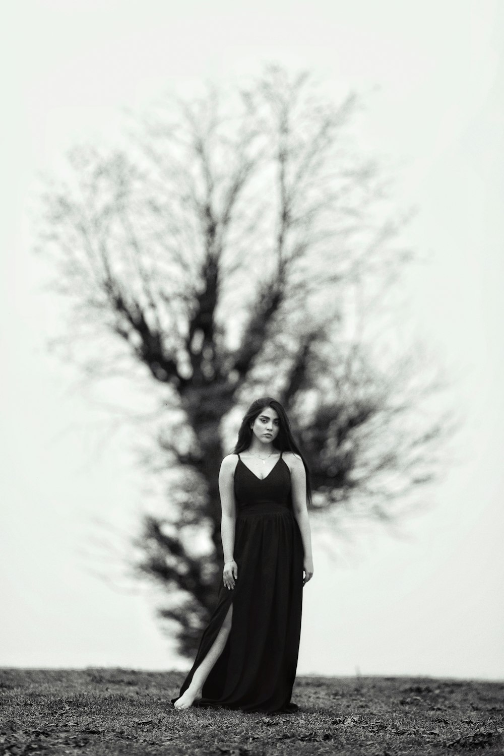a woman in a long black dress standing in front of a tree