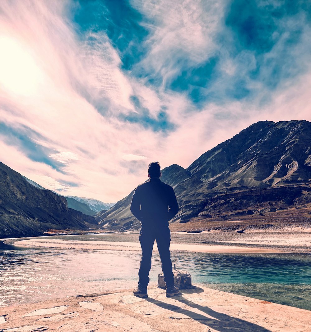 a man standing on a rock next to a body of water