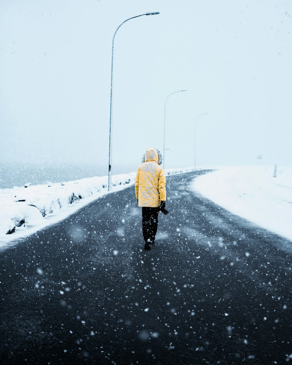 uma pessoa em uma jaqueta amarela andando por uma estrada nevada