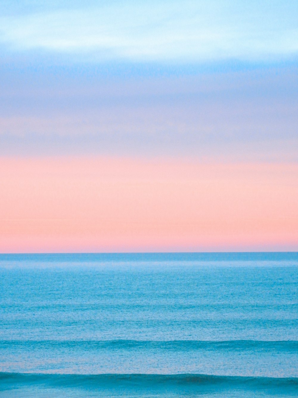 a lone surfboard sitting on the beach in front of the ocean