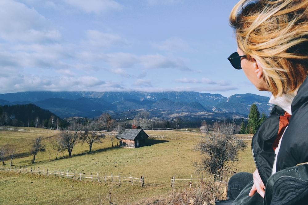 a woman looking out over a field with mountains in the background