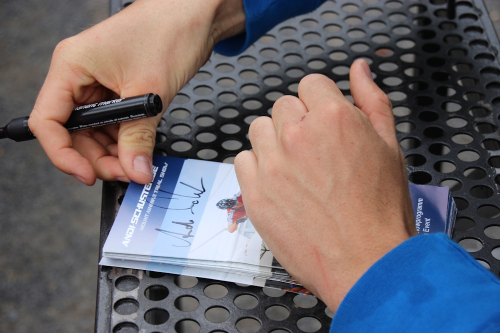 a person holding a pen and a book on a table